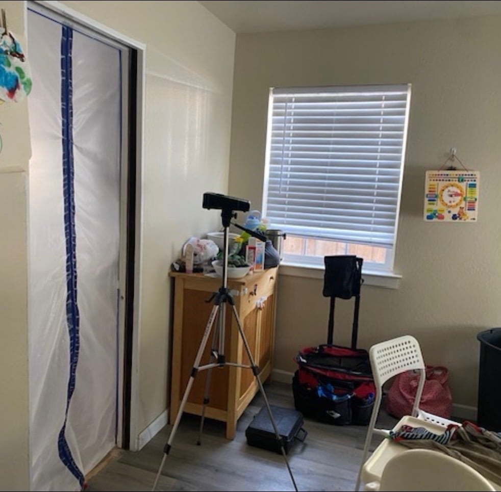 Home gym corner with stationary exercise bike, wooden stand with equipment, window with blinds, and storage items